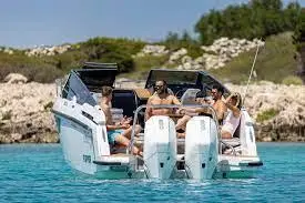 A group of five people enjoying a day on a motorboat in clear blue water, surrounded by rocky shoreline and greenery.